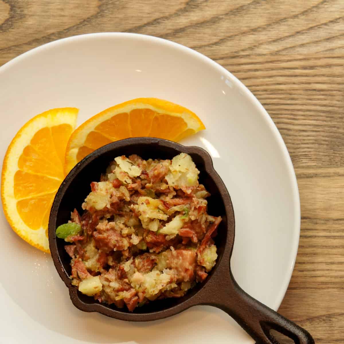 Corned bee hash being served in a small skillet along with an orange garnish.