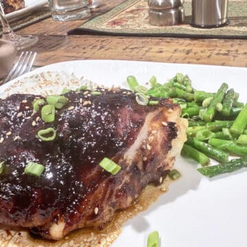 A plate of Hoisin chicken thighs with ebony skin and green asparagus.