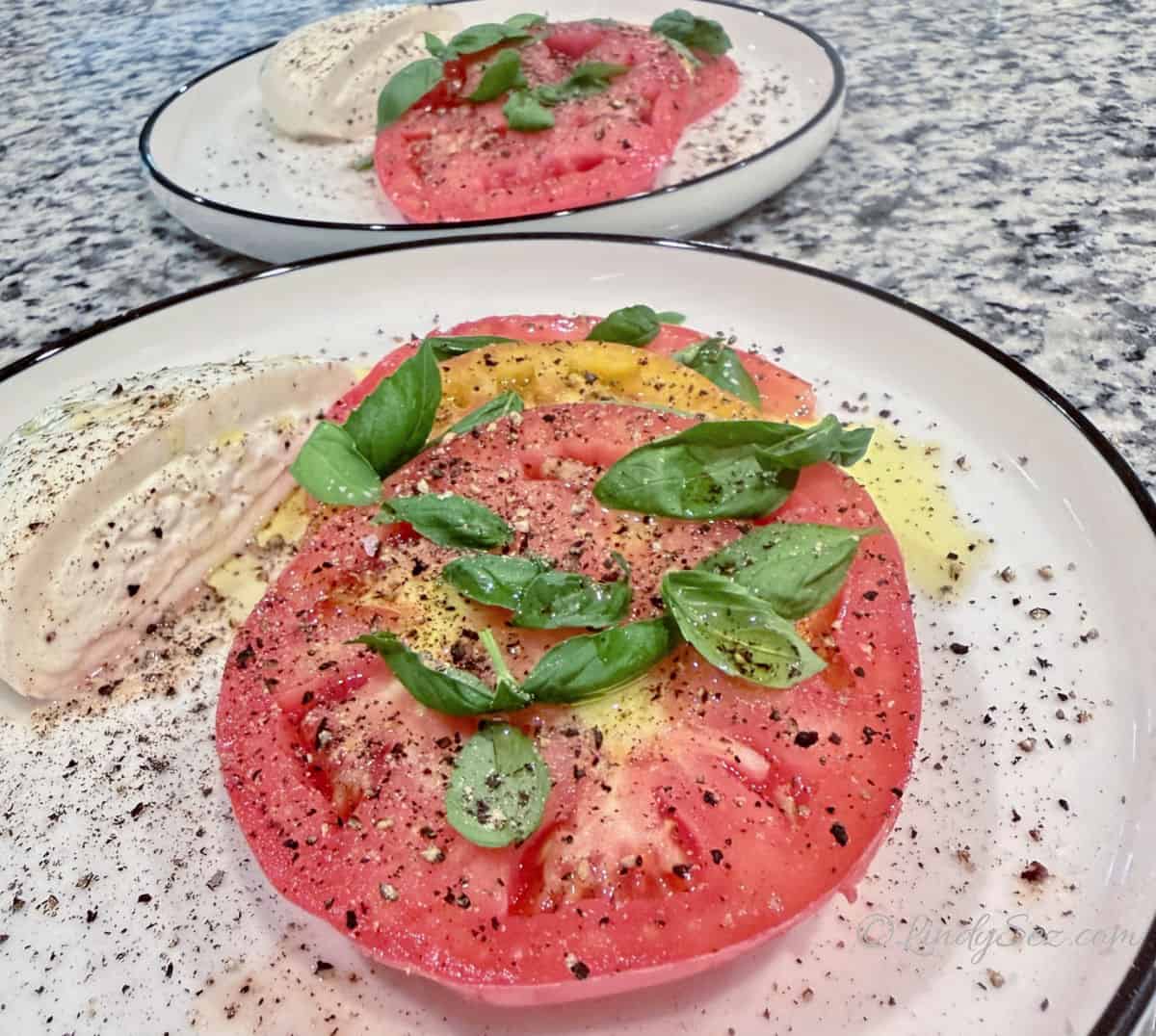 A close up view of a tomato sitting on a buratta caprese salad.