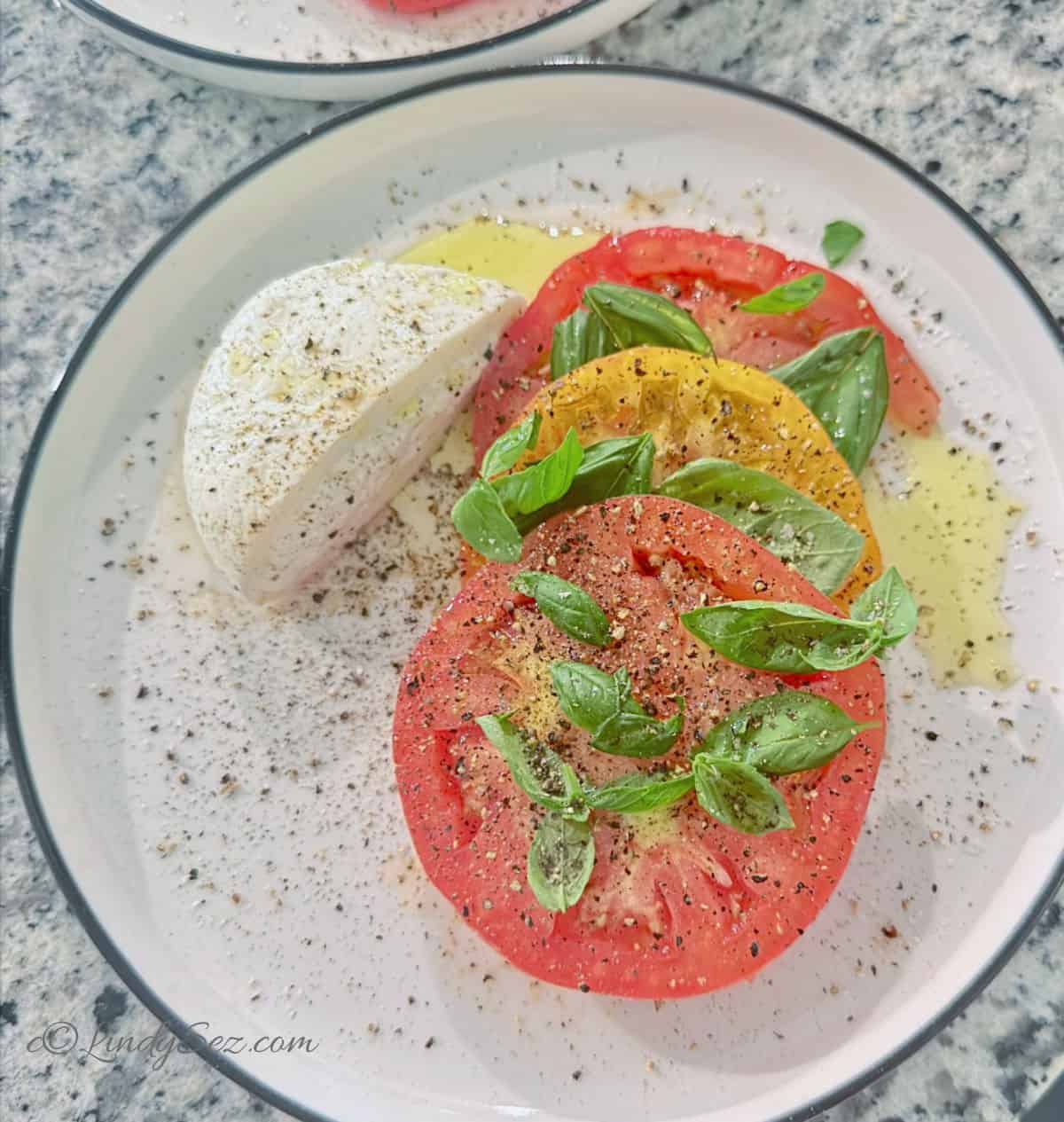 Caprese Buratta Salad with heirloom tomatoes on a plate with extra virgin olive oil and a lot of pepper.