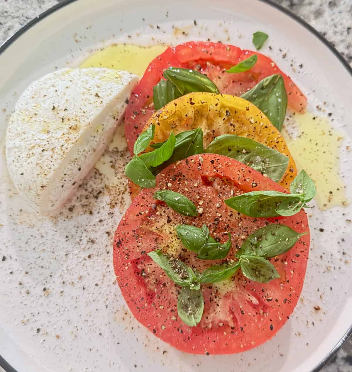 A plate with red and yellow tomato, basil, extra virgin oliv oil, and a hlaf baratta ball.