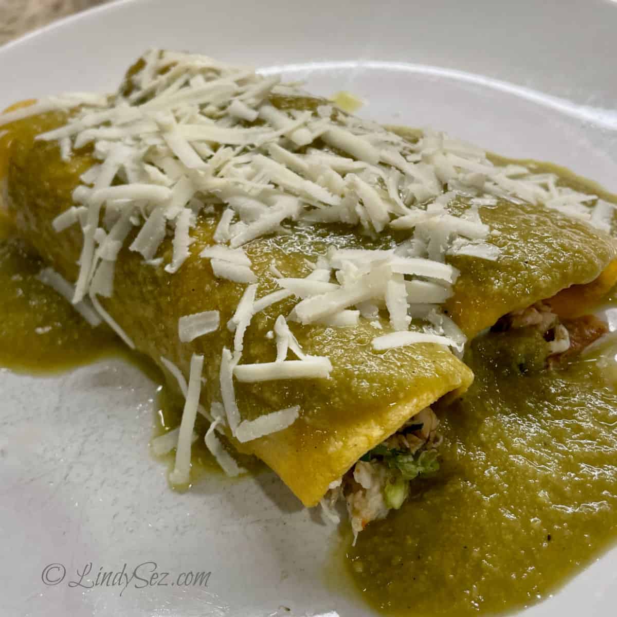 A plate with two crab enchiladas with green sauce.