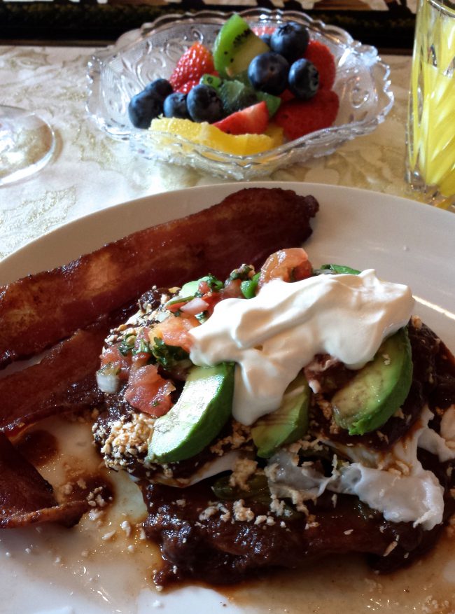 Lindy's Ultimate Huevos Rancheros on a plate with fruit behind.was shot by Helen