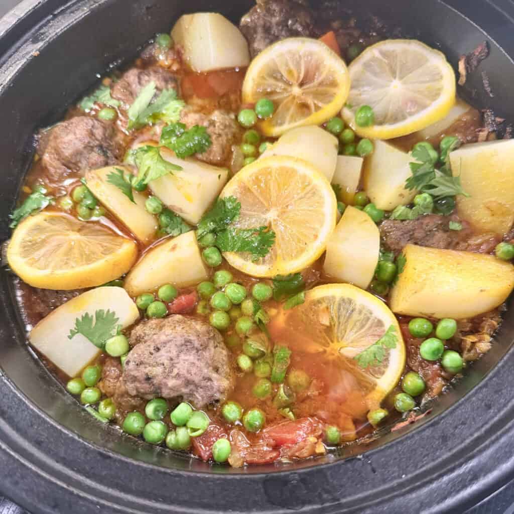 An open tagine filled with potatoes, peas, and kefta meatballs. 