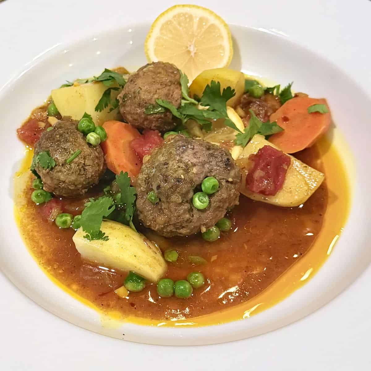 A bowl of beef and lamb meatballs (kefta) in a broth with potatoes, carrots, and peas.