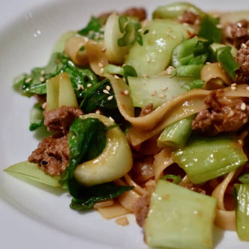 Bok Choy and ground lamb simmer in a sauce and are served over noodles in a white bowl.