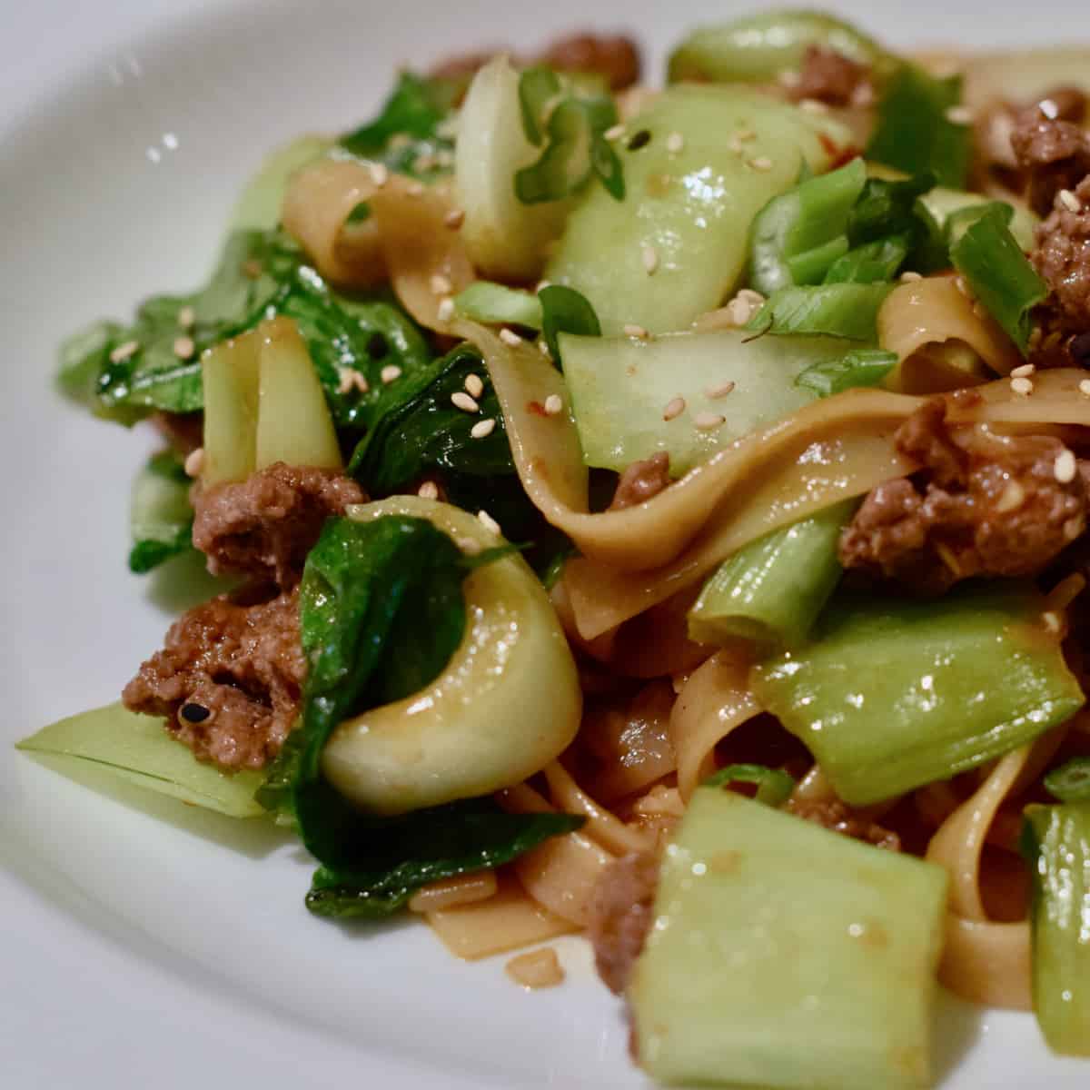 Bok Choy and ground lamb simmer in a sauce and are served over noodles in a white bowl.