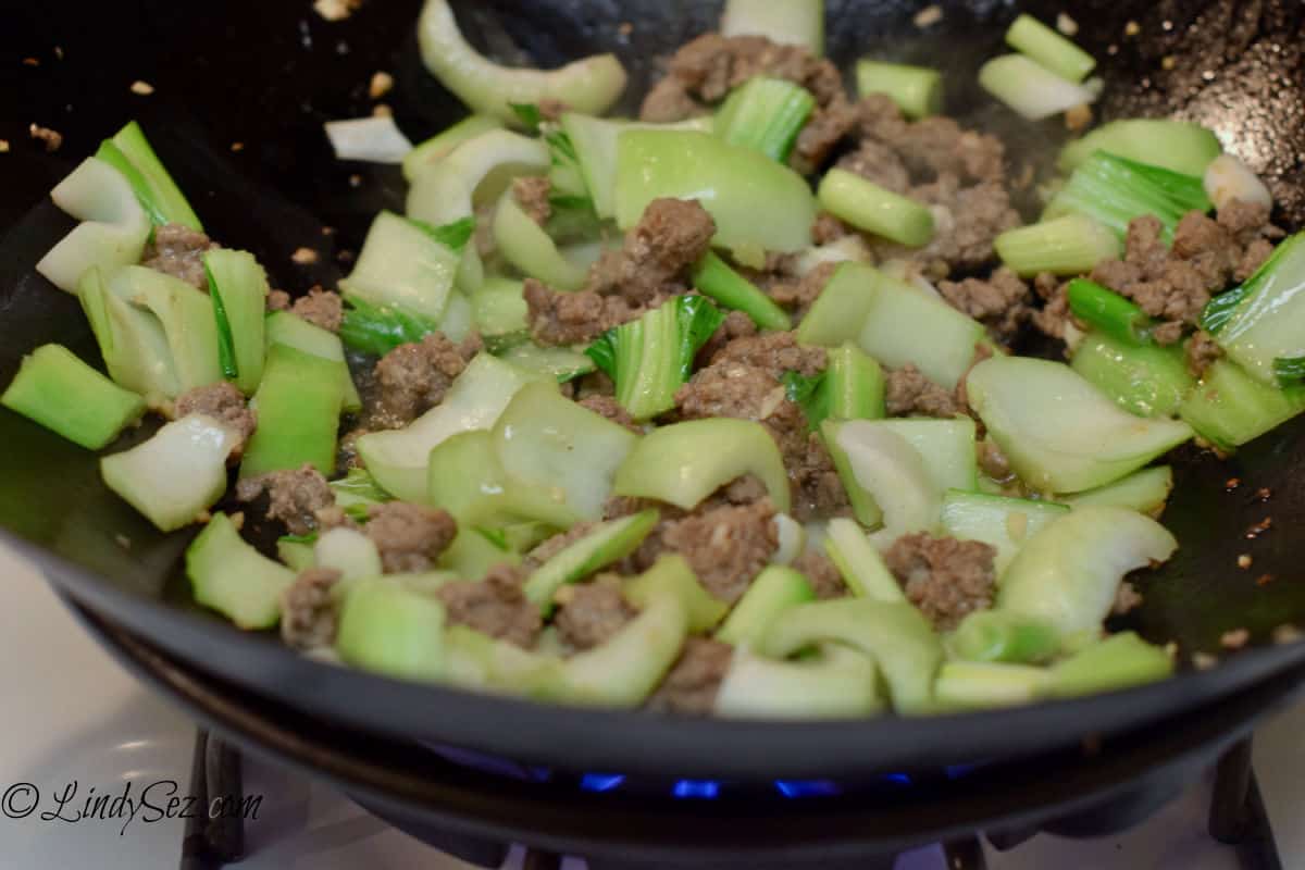 A wok with ground lamb and bok choy being stir-fried together.