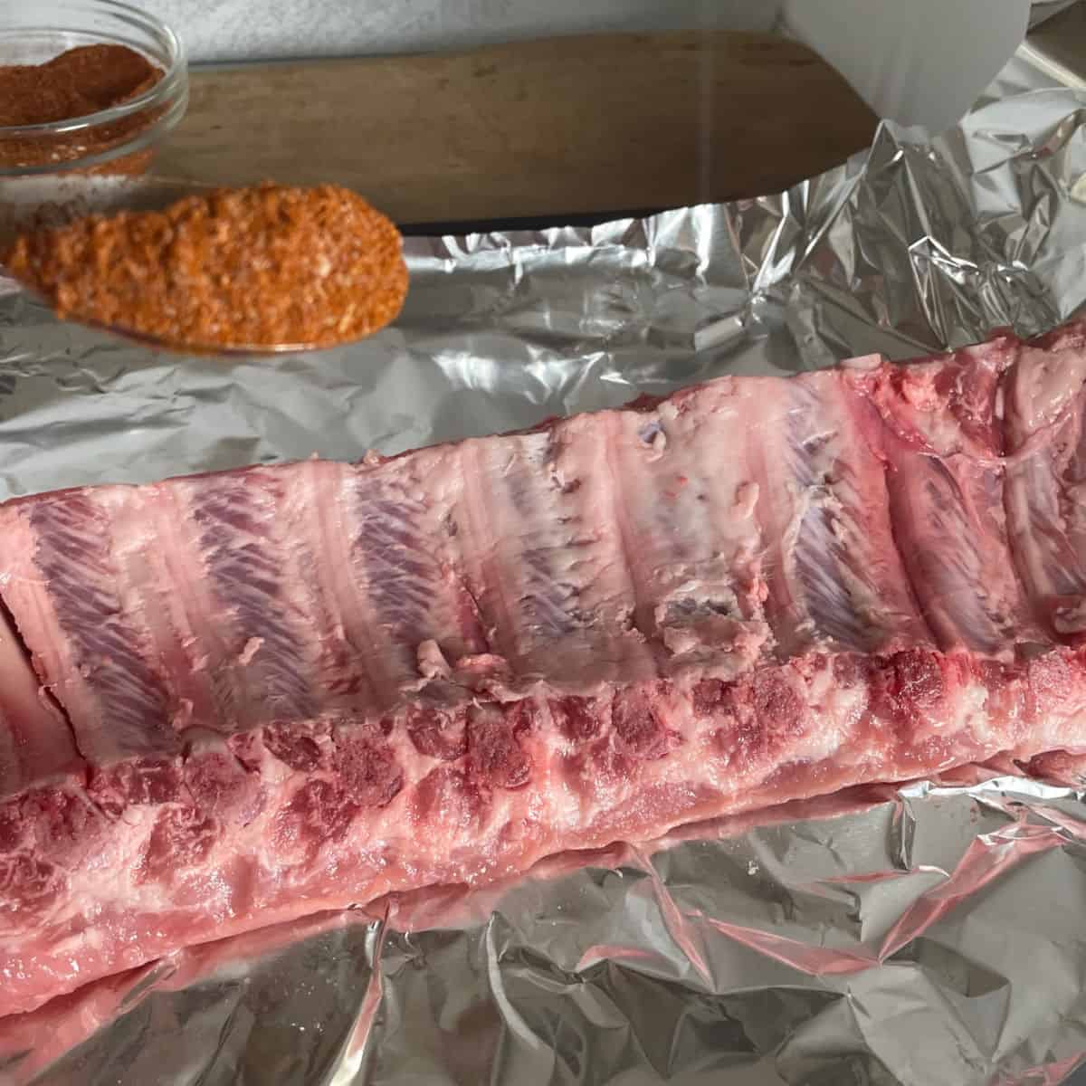 A rack of baby back ribs and a spoonful of seasoning mix on aluminum foil.