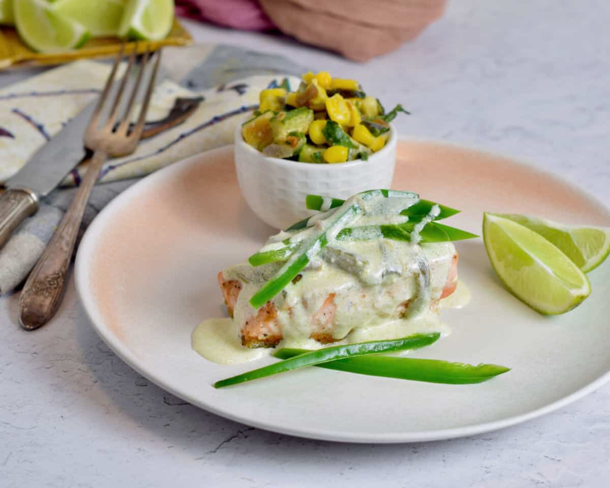 A plate with salmon with a jalapeno cream sauce and a bowl of corn in the back. 