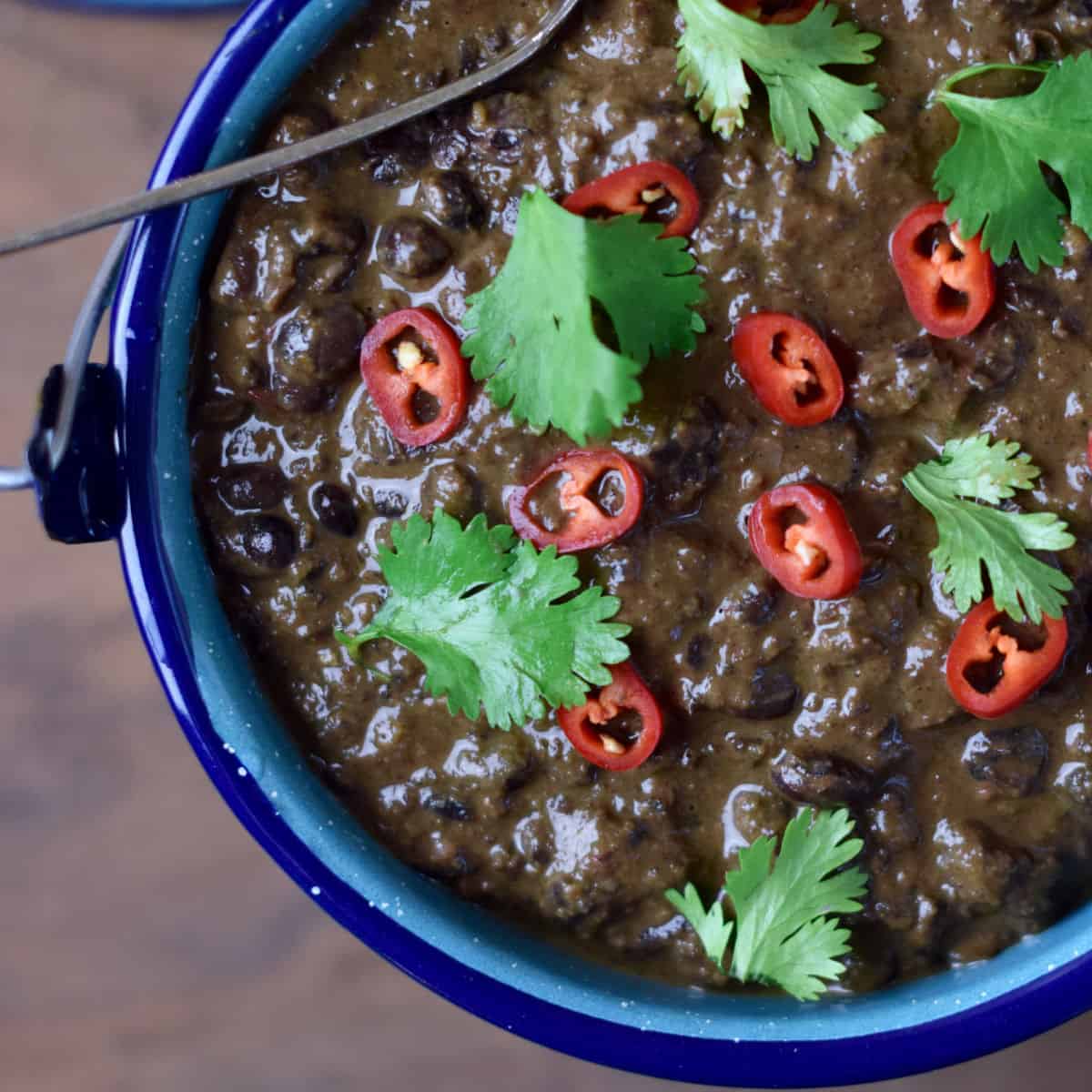 A blue pot holds Savory Black Beans with red chilies and cilantro on top.