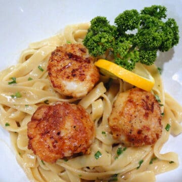 A bowl of lemony fehttuchini with 3 beautifully seared scallop.