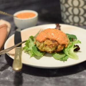 A delicious crab cake on a plate with salad and aoli.