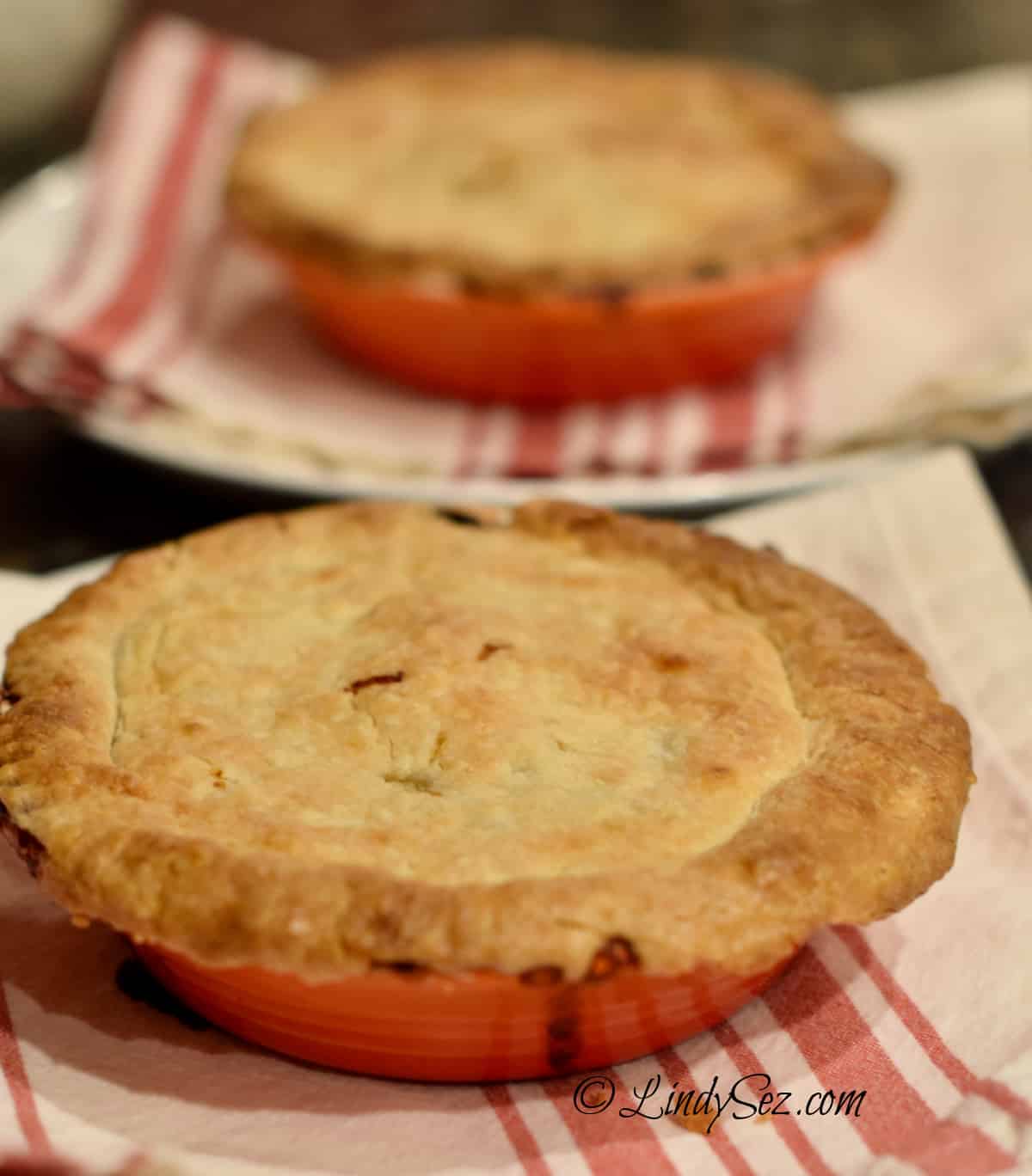 A pair of perfectly cooked pot pies in orange crocks.