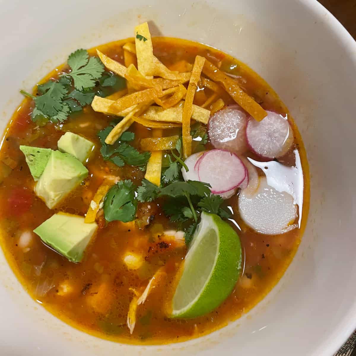 A bowl of red chicken tortilla soup with condiments. 