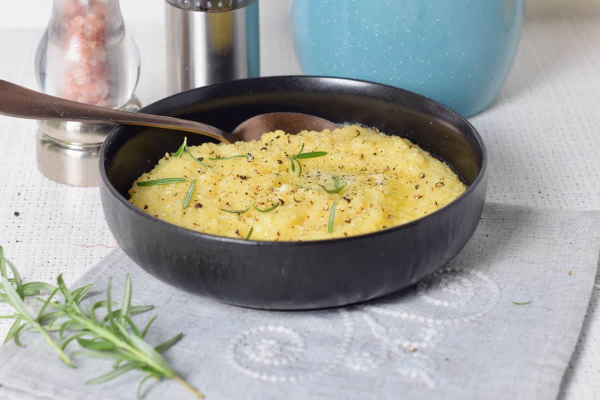 Creamy polenta in a black bowl with rosemary.