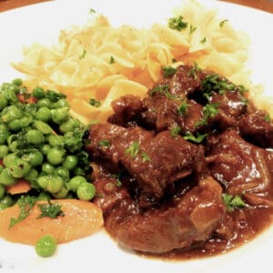 Beer-Braised Beef on a plate with peas and carrots.