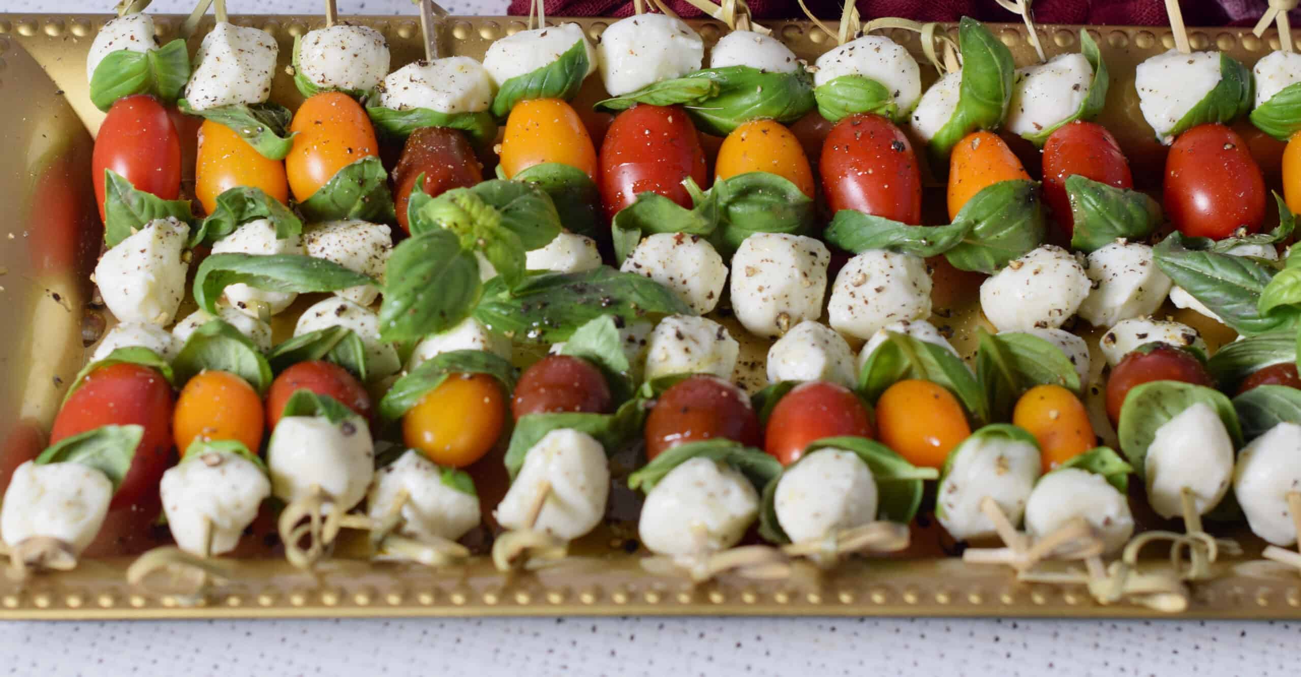 A plate holding cherry tomatoes, mozzarella balls, and basil, on a stick.