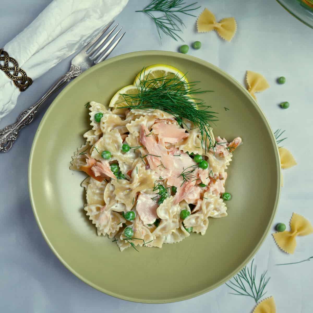 A green bowl holds a serving of Lemony Smoked Salmon Pasta with Peas.