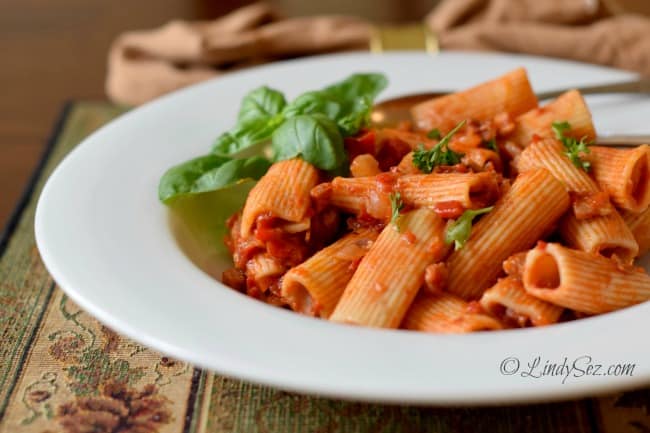 Rigatoni with Roasted Peppers, Tomatoes and Pancetta in a white bowl with basil leaves
