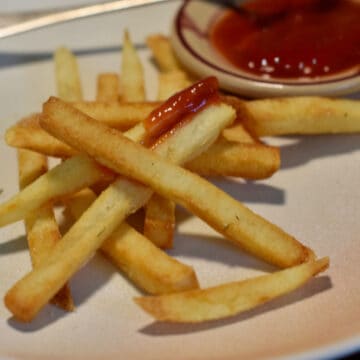 An image of French Fries with ketchup in the background ready for dipping.