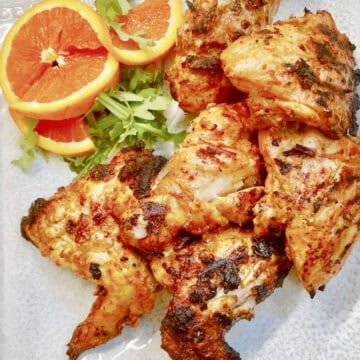 A platter of grilled Tandoori chicken with bright orange slices.