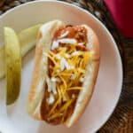 A hot dog dressed in chili gravy with pickles.