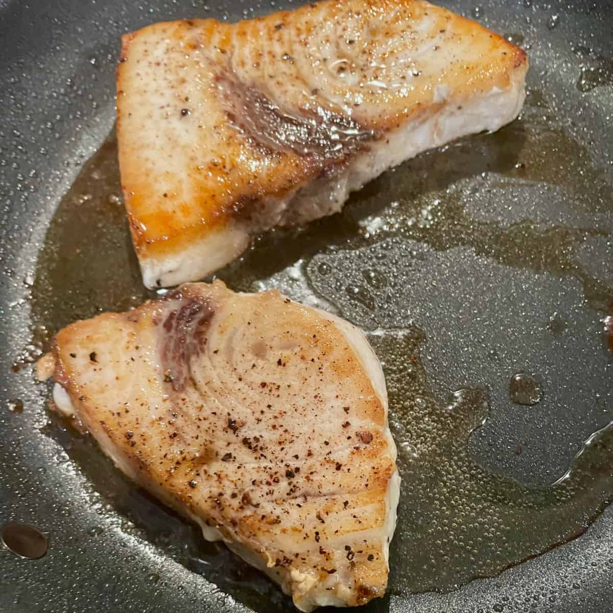 Out of the oven and perfectly cooked swordfish in a skillet.