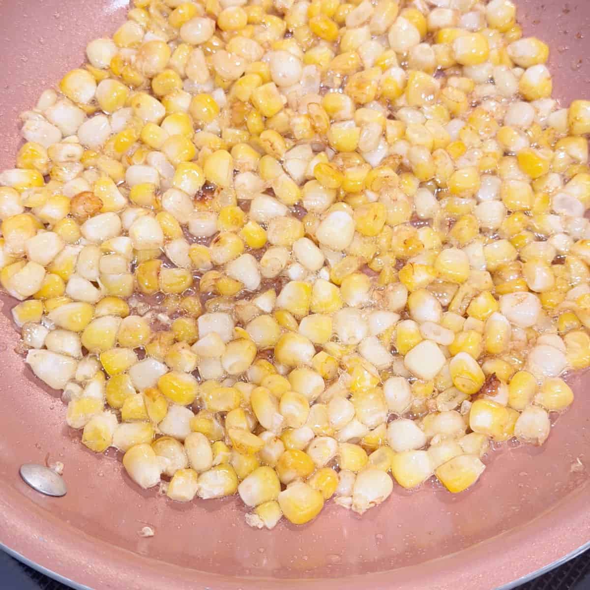 A copper pan with corn frying insdie.
