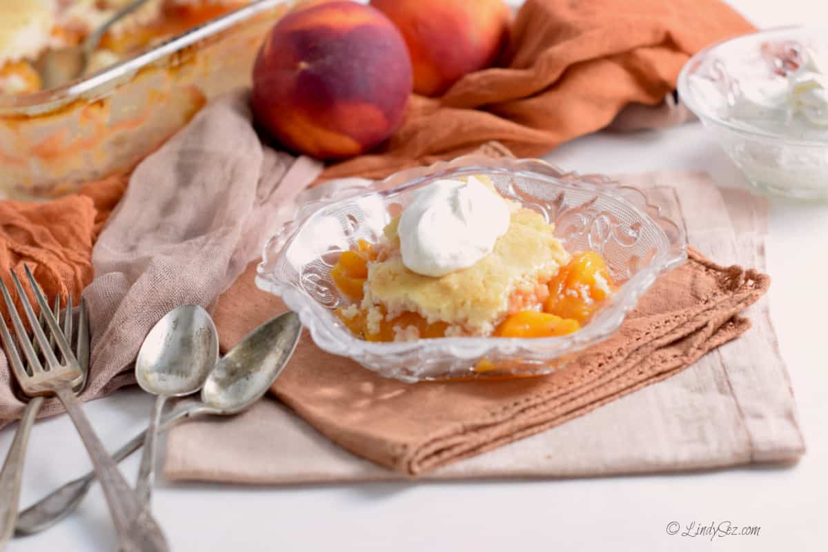 Peach cobbler with whipped topping in an antique glass bowl.