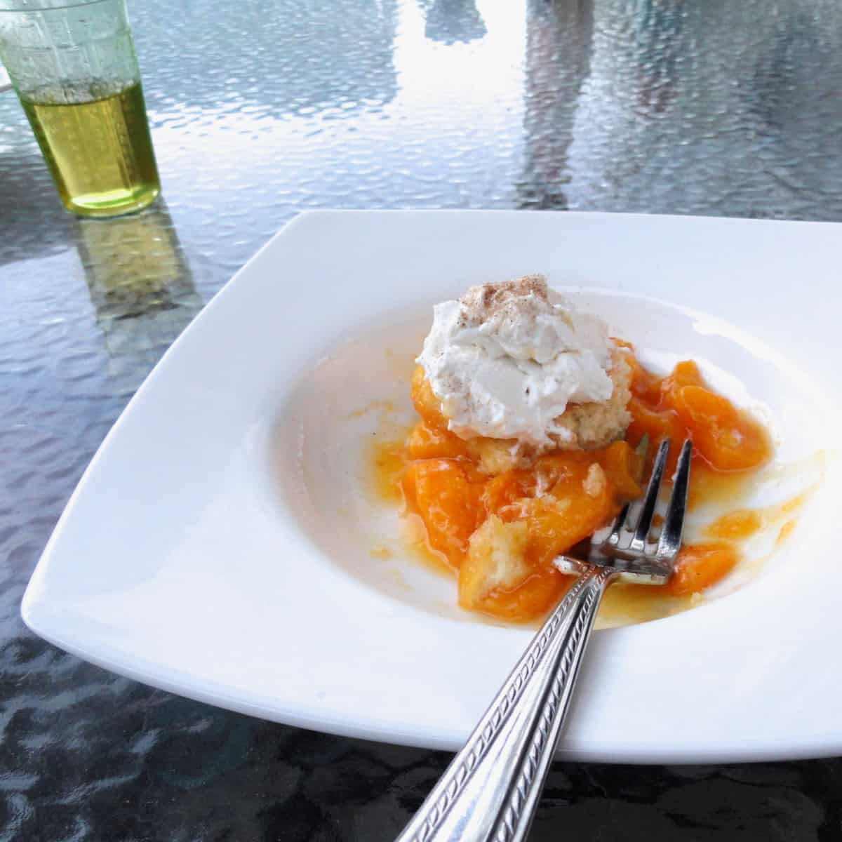 Peach cobbler being served in a small white bowl with whipped cream.
