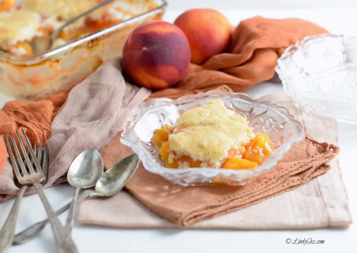 Colorful napkins and fresh peaches surround the dish of cobbler.