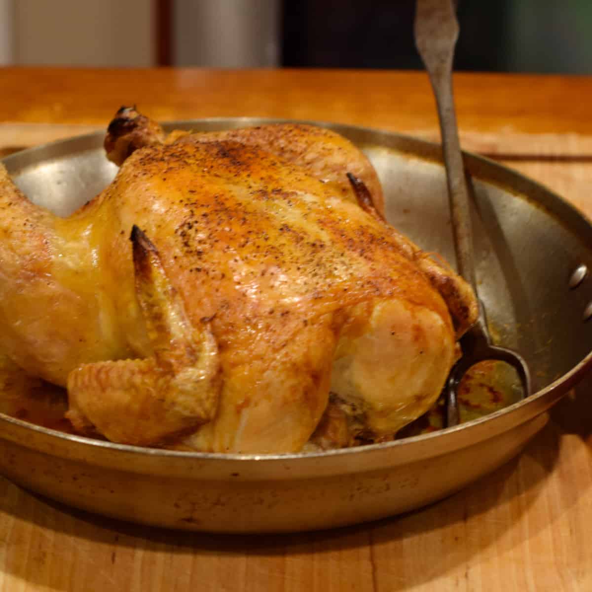 A perfect simple roast chicken is sitting in the pan with a fork.