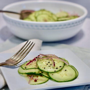 A bowl and plate of a simple cucumber salad with onions and cucumber.