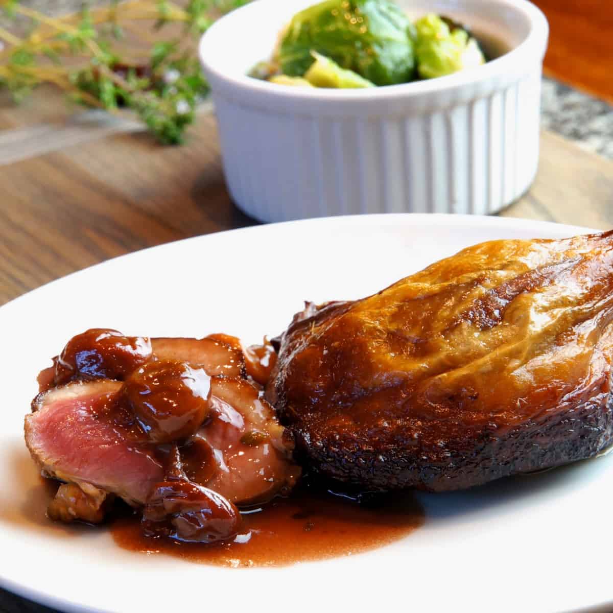 A perfectly rare slice of duck breast with a confit leg on a plate with port wine sauce. 