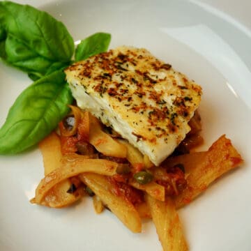 Halibut with Herbs and Fennel Tomato Sauce on a white plate with basil garnish.