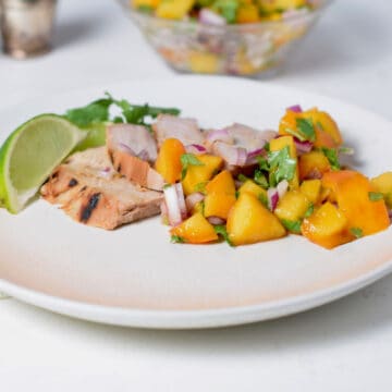 A plate of pork with salsa. A bowl of salsa sits behind.