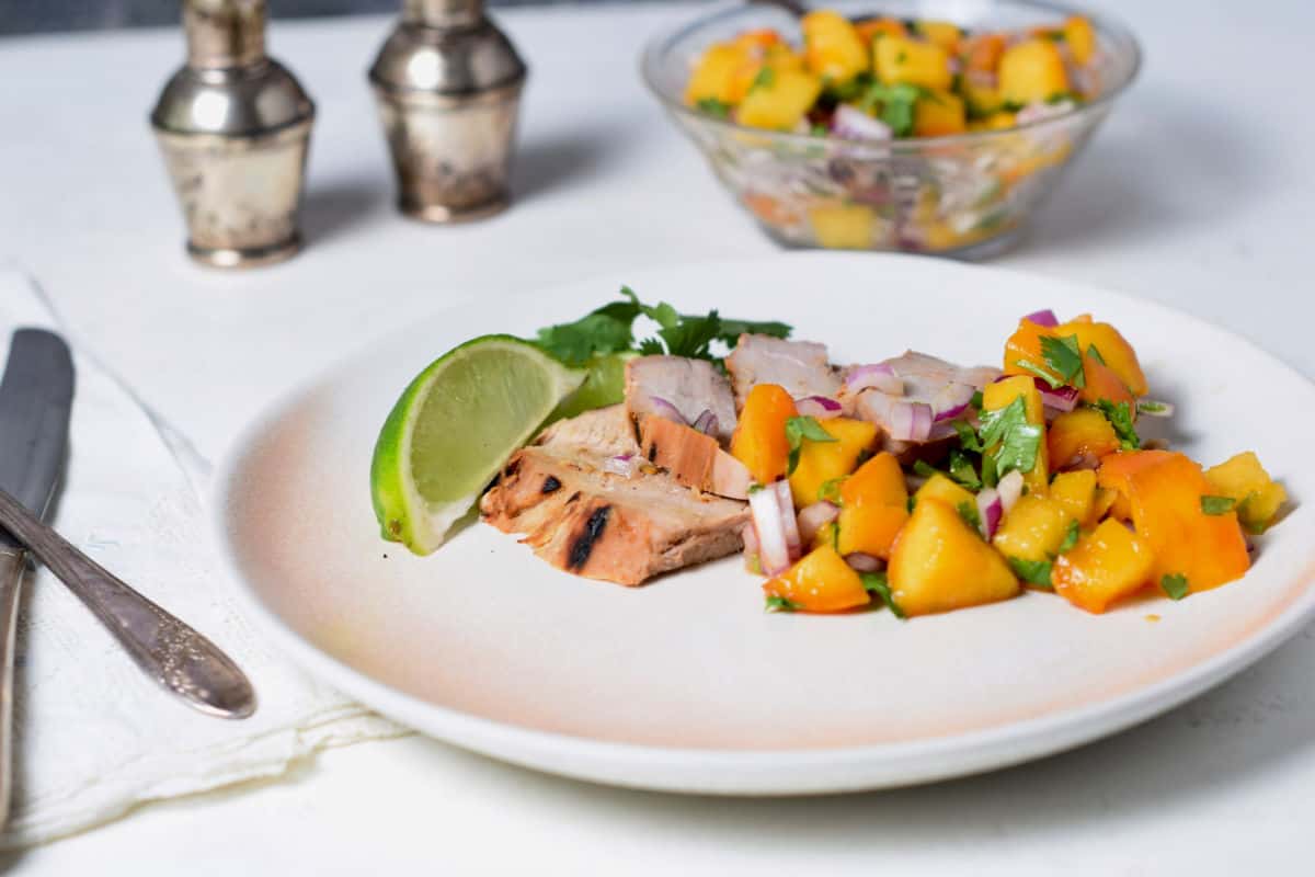 Pork Tenderloin with Fresh Peach Salsa on a plate with a dish of salsa behind.