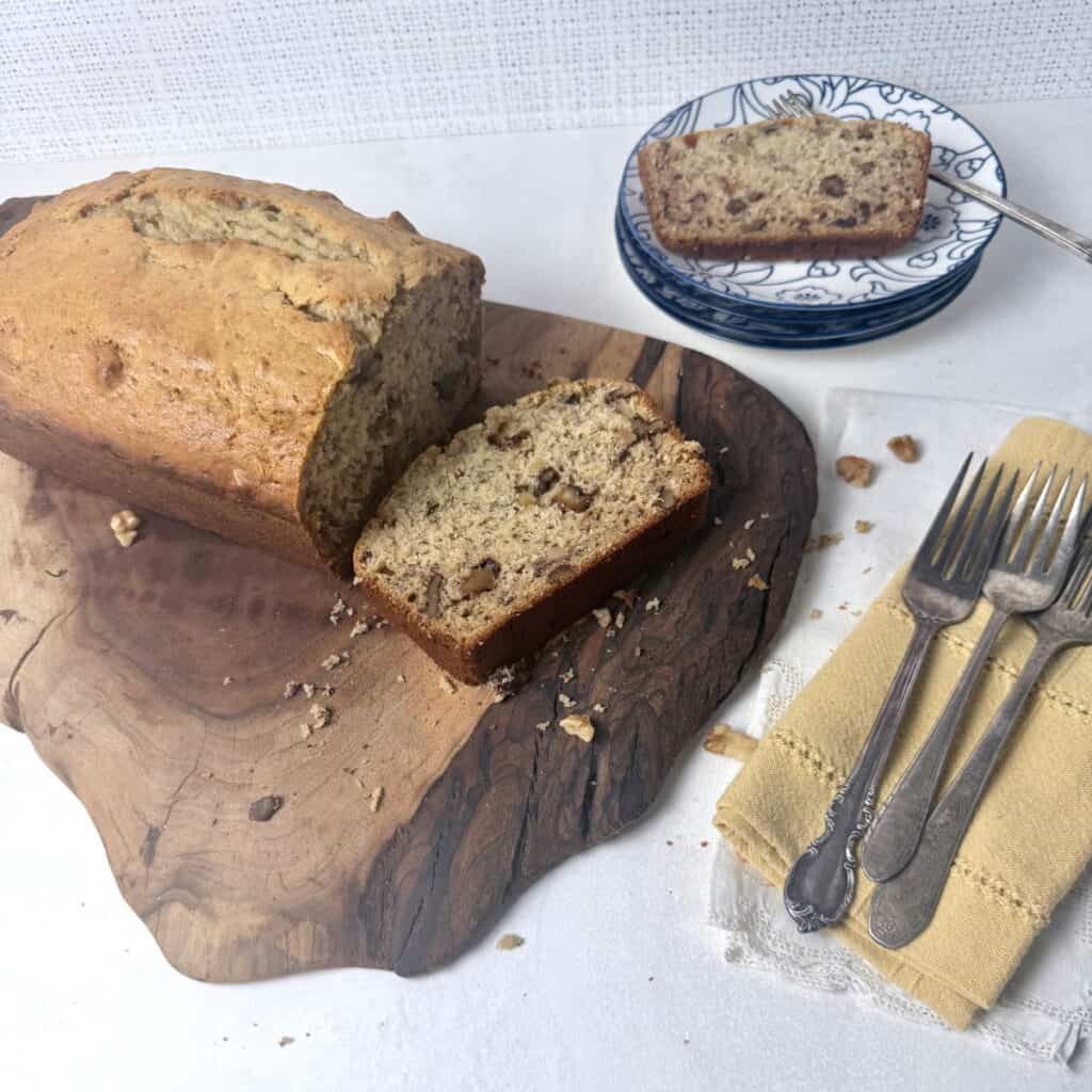 A loaf of old-fashioned banana bread on a cutting board with a slice of banana bread on a plate.