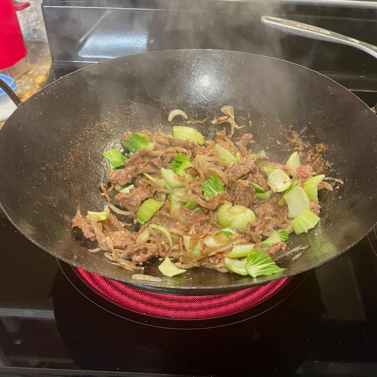 A wok with meat, onions and baby bok choy.
