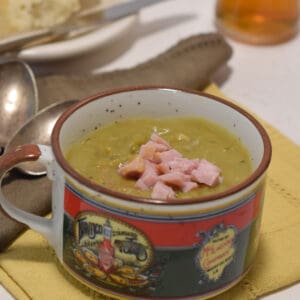 Chopped pieces of ham sit on top of a bowl of split pea soup.