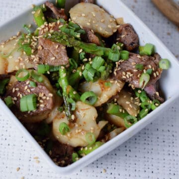 A white square bowl holding beef and scallop stir-fry with asparagus.