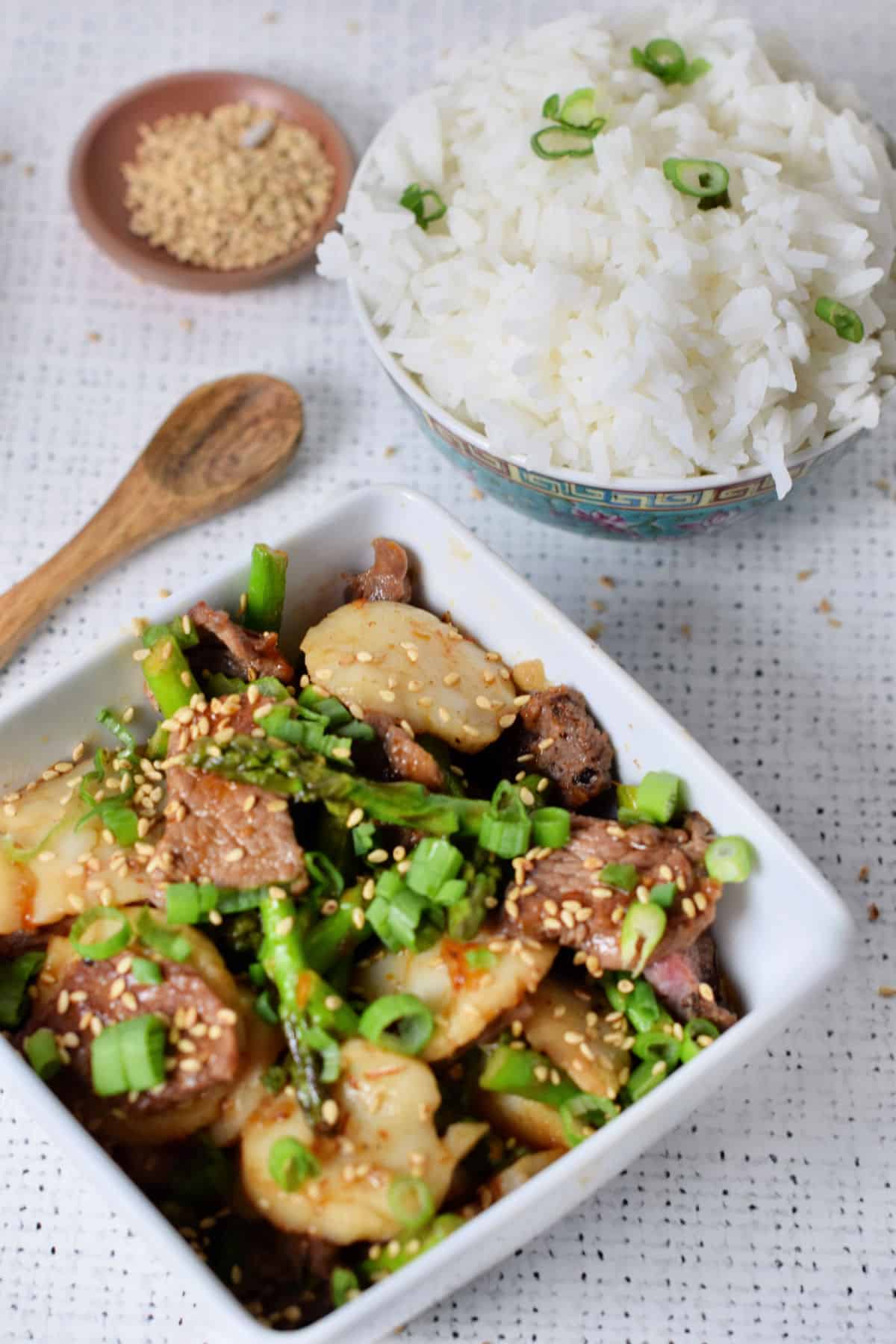 Rice in a bowl, beef with scallops in a second bowl with sesame seeds in another little bowl.