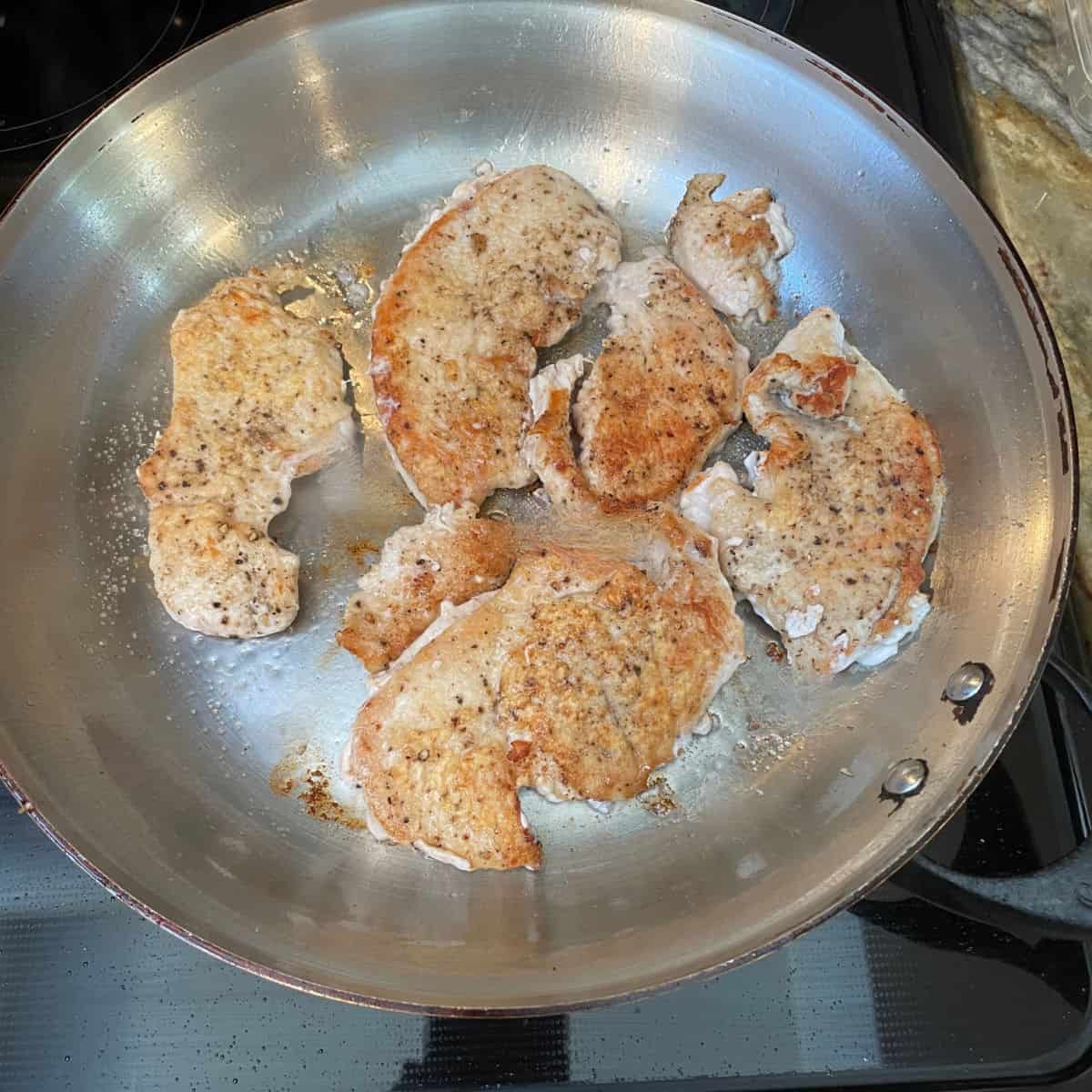 A frying pan with browned turkey cutlets.