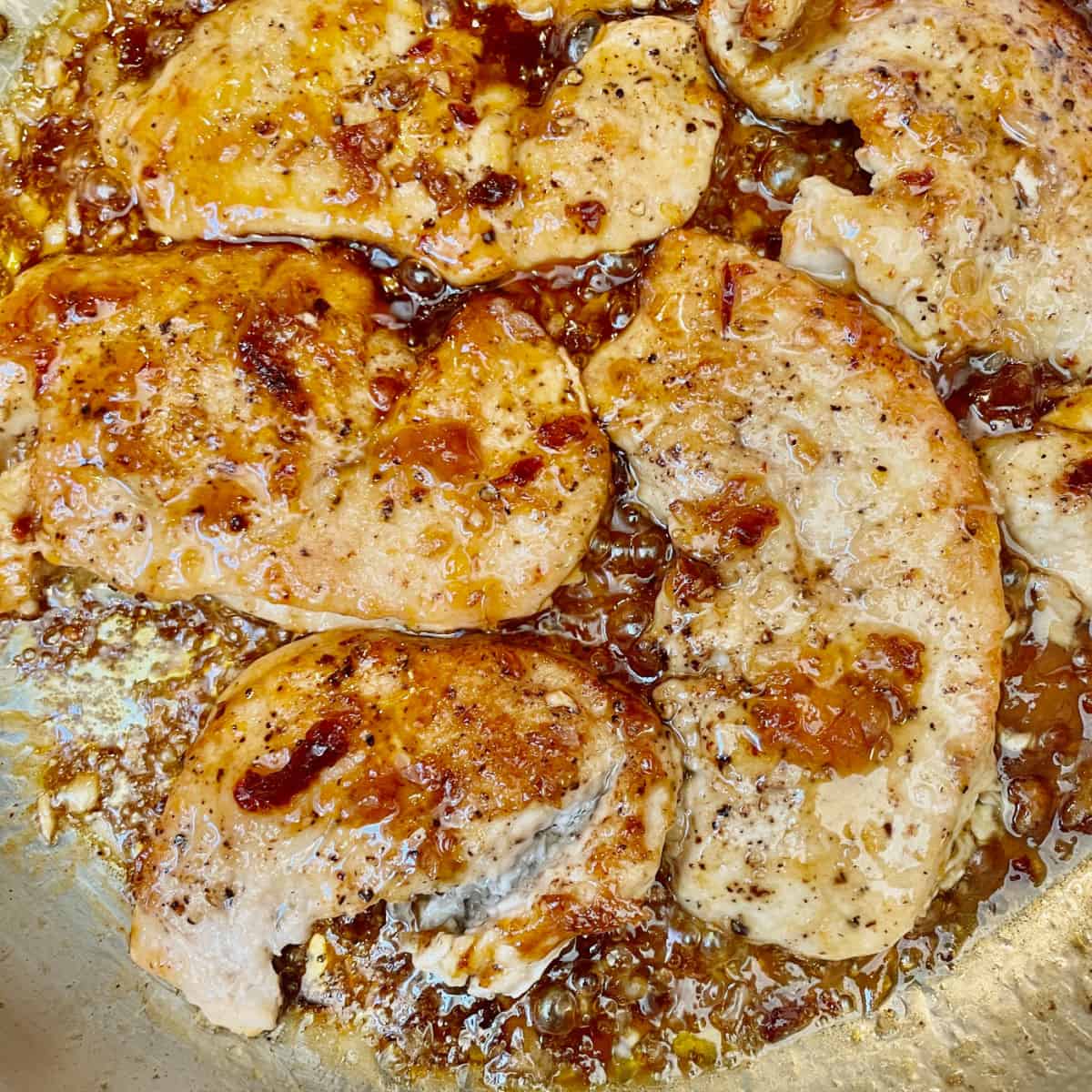 Glazed cutlets in the pan being tossed in sauce.