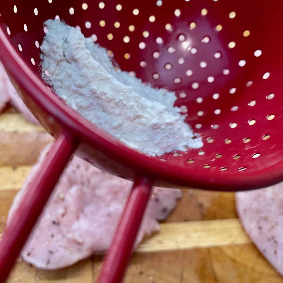Using a strainer to put flour onto meat. 