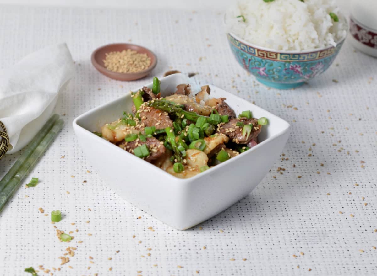 Beef and scallops in a bowl with rice and sesame seeds.