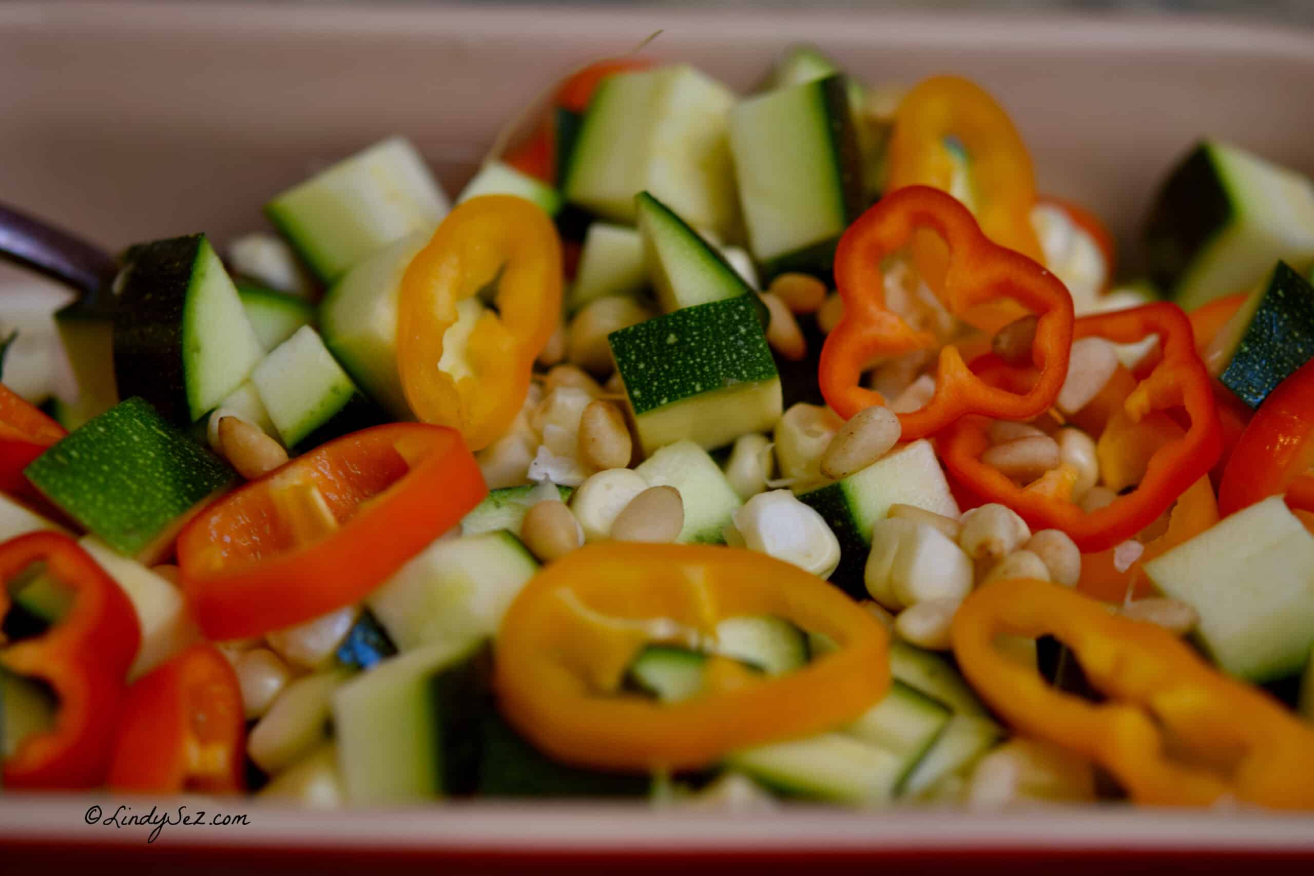 A bowl of prepared ingredients needed to make a fresh corn and zucchini saute with peppers and pine nuts.