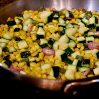 A bright and colorful pan with zucchini corn saute in it.