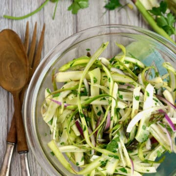 Shaved asparagus salad in A glass bowl with wooden fork and spoon.